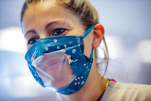 Woman wearing face mask with clear plastic window cut through it, so that you can see her mouth.